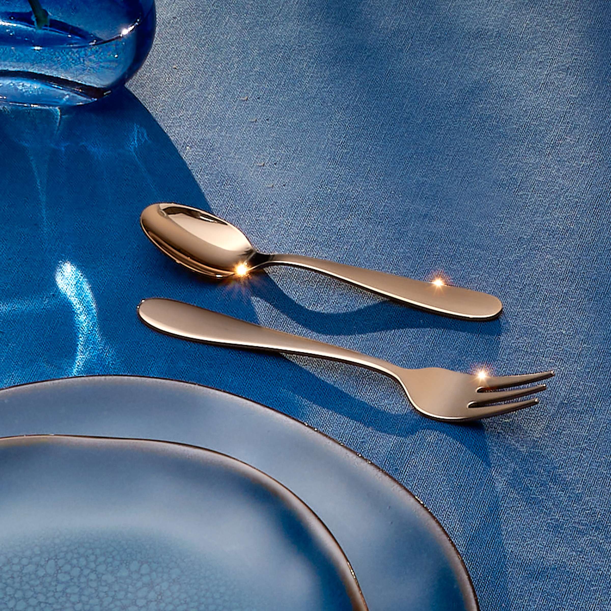 Amefa Oxford Besteckset 24-teilig mit PVD kupfer-finish, Messer, Gabeln, Löffel und Teelöffel, auf dunkelgrauem Hintergrund.