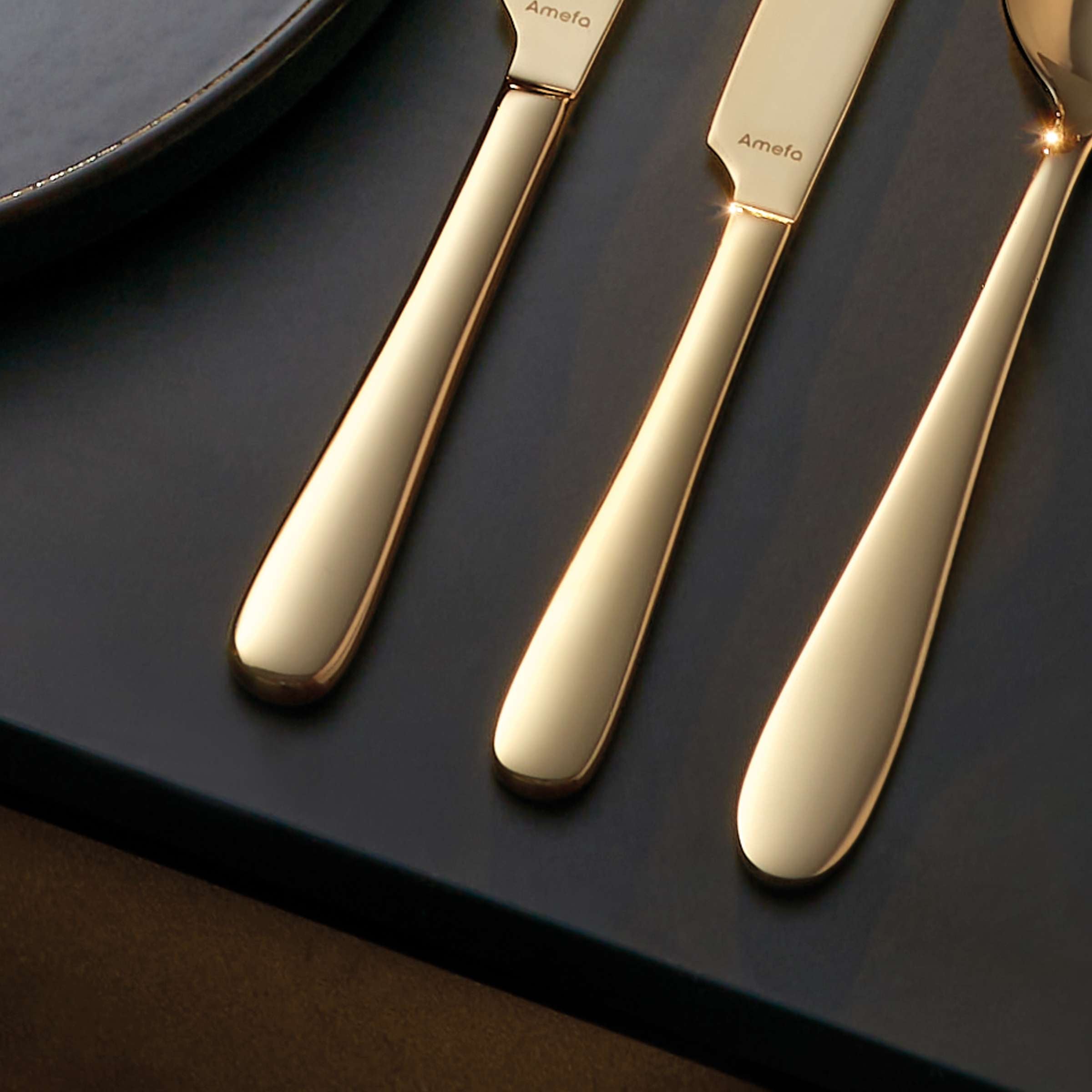 Amefa Oxford Besteckset 24-teilig in Champagner PVD, Besteck mit Messer, Gabel, Löffel auf dunklem Hintergrund sichtbar
