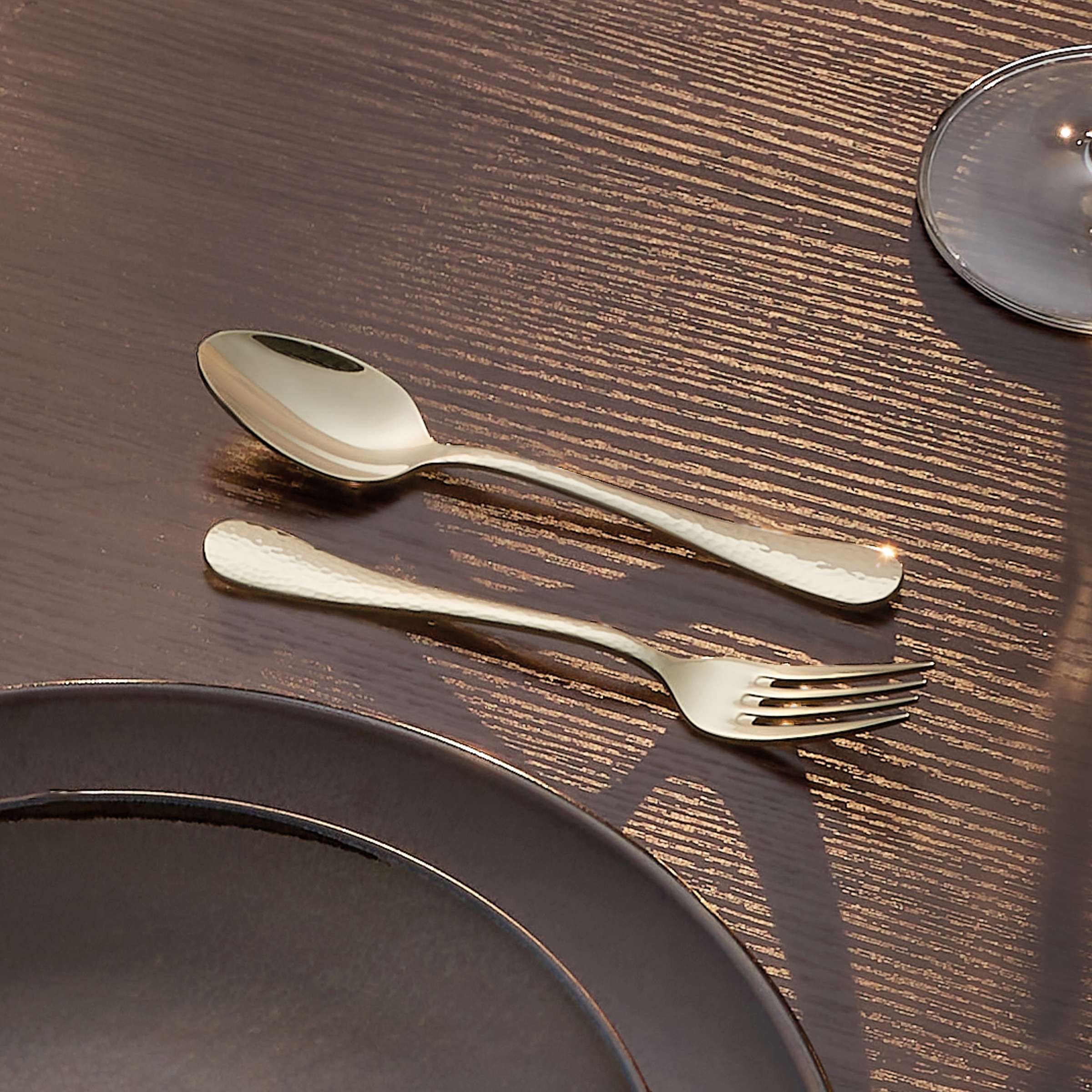Amefa Sierra Besteckset 30-teilig aus PVD-Champagner mit Messer, Gabel, Löffel und Teelöffel auf dunklem Hintergrund.