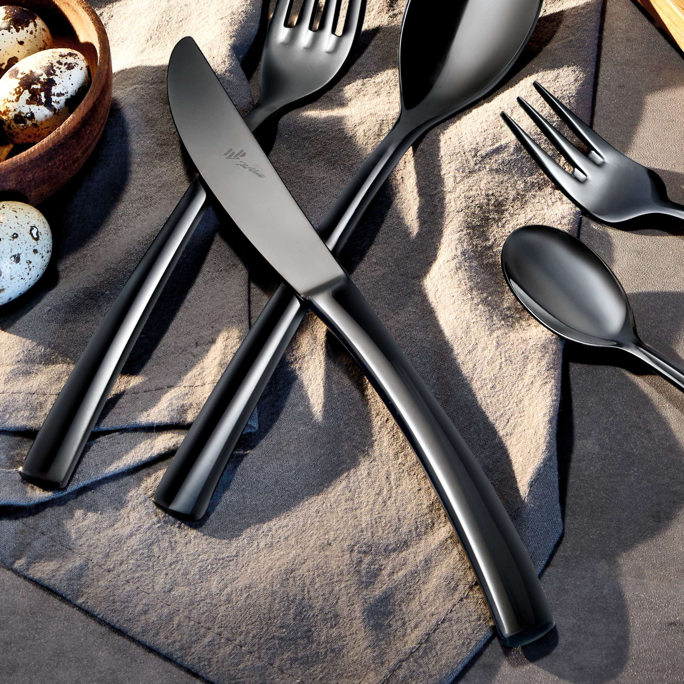 Schwarzes SWING Besteckset 24-teilig von Paul Wirths, aus PVD-beschichtetem Edelstahl, zeigt Messer, Gabeln und Löffel auf dunklem Hintergrund.